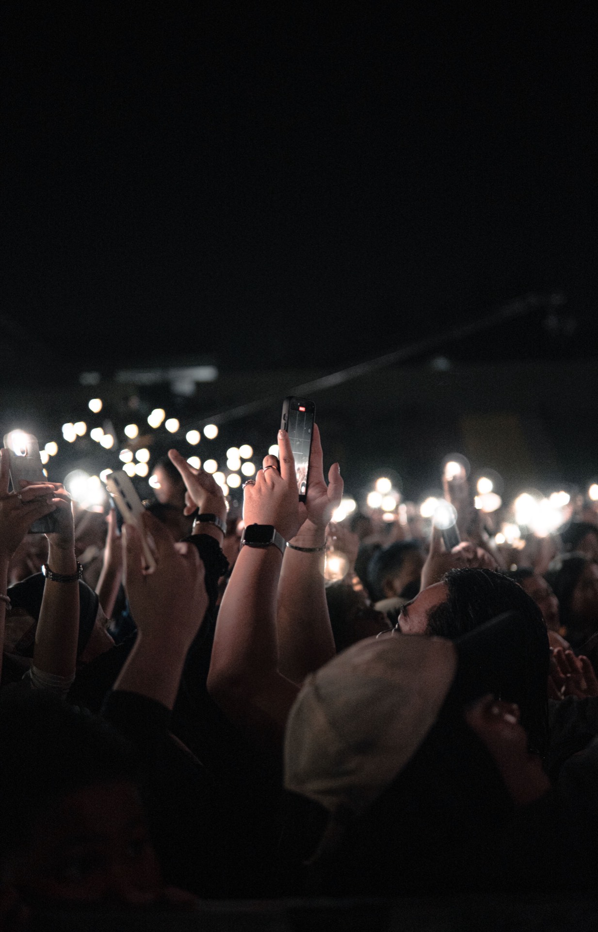 A concert crowd holding up glowing phones as flashes light the night